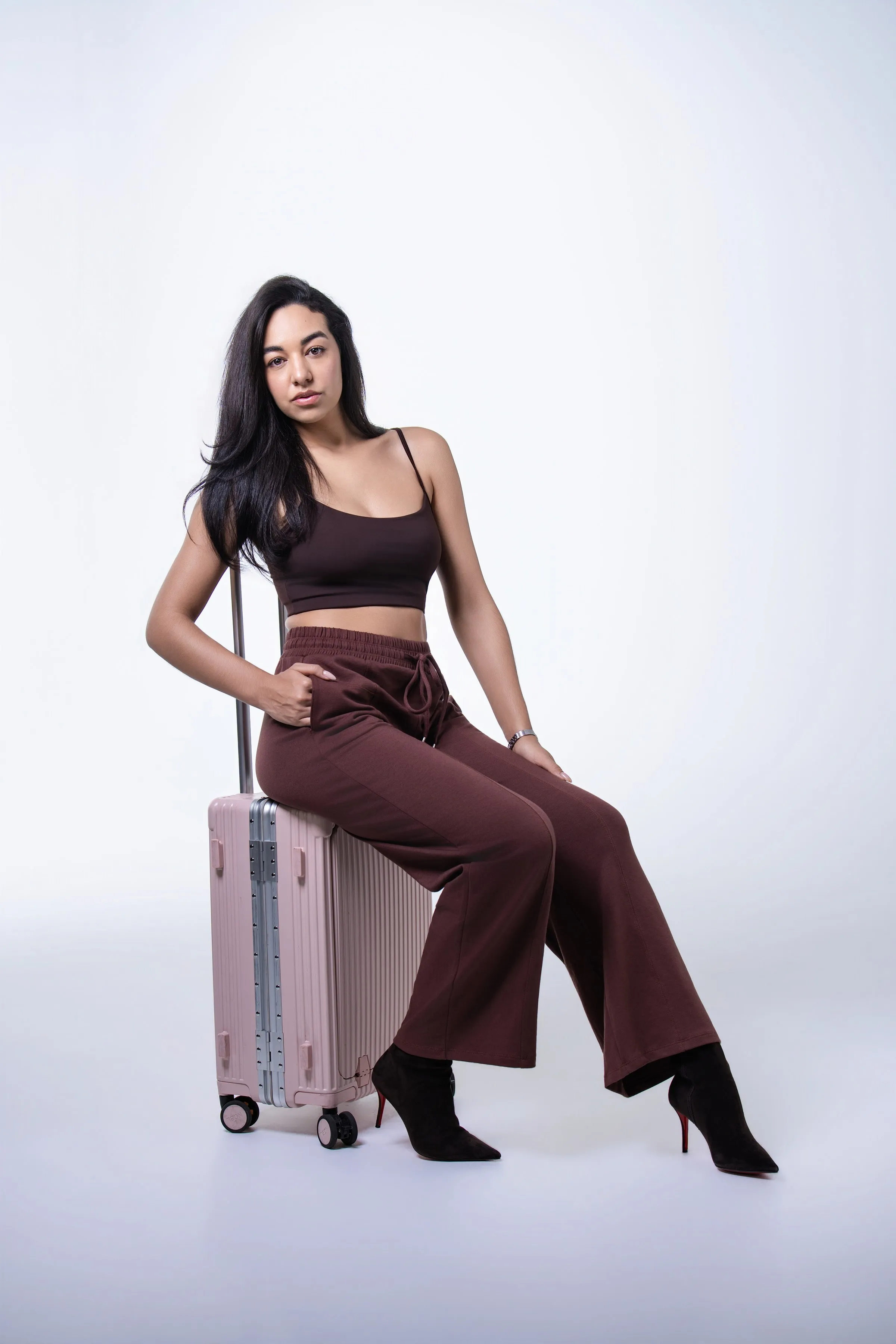Model in a burgundy co-ord seated on a pink carry-on suitcase